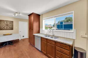 Kitchen featuring dishwasher, a sink, tasteful backsplash, light wood finished floors, and brown cabinetry