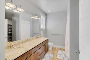 Full bath featuring double vanity, wood finished floors, toilet, baseboards, and a shower with curtain
