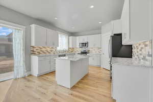 Kitchen featuring stainless steel appliances, a center island, backsplash, light wood-style flooring, and recessed lighting