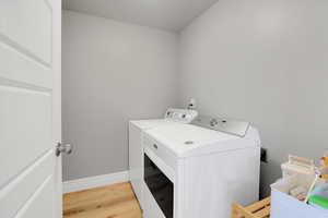 Washroom with independent washer and dryer, light wood finished floors, and baseboards