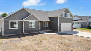 View of front of house with stone siding, driveway, a garage, and a shingled roof
