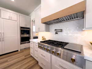 Kitchen featuring custom range hood, appliances with stainless steel finishes, light countertops, backsplash, and white cabinetry