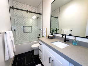 Bathroom with vanity, toilet, combined bath / shower with glass door, and marble look tile flooring