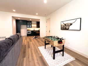 Rec room with bar with sink, light wood-style floors, recessed lighting, and baseboards