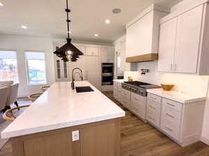 Kitchen with appliances with stainless steel finishes, a sink, light wood-style floors, recessed lighting, and premium range hood