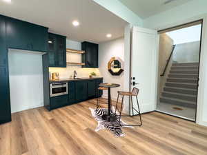 Kitchen with oven, light wood-style flooring, glass insert cabinets, recessed lighting, and a sink