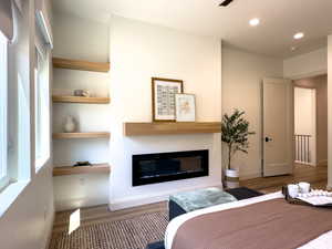 Bedroom with a glass covered fireplace, wood finished floors, recessed lighting, and baseboards