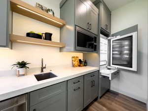 Kitchen featuring open shelves, a sink, stainless steel microwave, gray cabinetry, and dark wood-type flooring