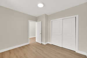 Unfurnished bedroom with light wood-style floors, baseboards, and a closet