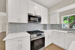 Kitchen with stainless steel appliances, light wood-style flooring, light countertops, white cabinetry, and backsplash