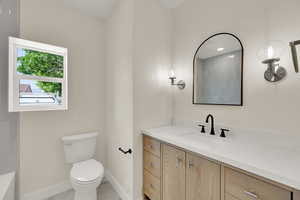 Full bathroom with vanity, toilet, baseboards, a tub to relax in, and marble look tiles