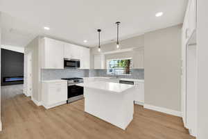 Kitchen with stainless steel appliances, a sink, backsplash, light wood-style floors, and white cabinetry