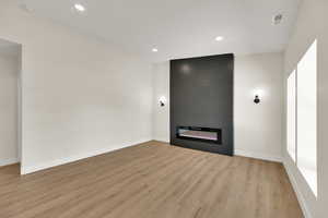 Unfurnished living room featuring light wood-style floors, baseboards, a fireplace, and recessed lighting