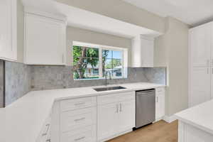 Kitchen featuring dishwasher, a sink, light countertops, light wood-style floors, and white cabinetry