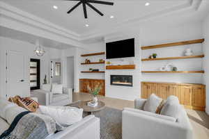 Living area with light wood-style flooring, recessed lighting, a raised ceiling, a fireplace, and a ceiling fan