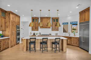 Kitchen with stainless steel appliances, a sink, brown cabinetry, backsplash, and a center island with sink