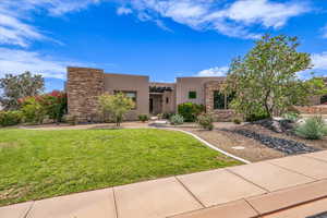 Pueblo revival-style home featuring stucco siding, a front lawn, and stone siding