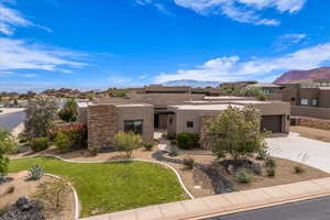 Pueblo-style house with stucco siding, a mountain view, driveway, an attached garage, and a front lawn