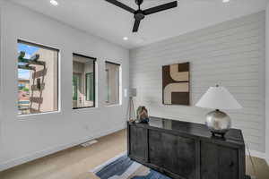 Office space featuring ceiling fan, light wood finished floors, baseboards, recessed lighting, and wooden walls