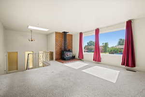Unfurnished living room with a chandelier, carpet, a skylight, and a wood stove