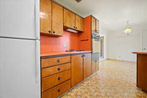 Kitchen with white appliances, brown cabinetry, light countertops, brick patterned flooring, and a warming drawer