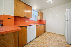 Kitchen with white appliances, a sink, light countertops, tasteful backsplash, and brown cabinetry