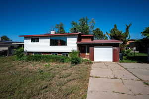 Split level home with concrete driveway, an attached garage, and a chimney