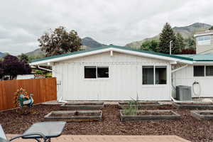 Rear view of property with board and batten siding, cooling unit, a mountain view, and a garden
