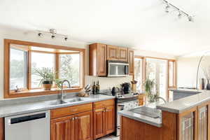 Kitchen with stainless steel appliances, a sink, rail lighting, brown cabinets, and glass insert cabinets
