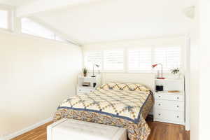 Bedroom with wood finished floors, lofted ceiling, and baseboards