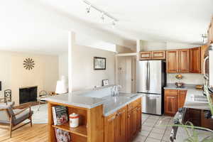 Kitchen featuring freestanding refrigerator, vaulted ceiling, rail lighting, a sink, and light stone countertops