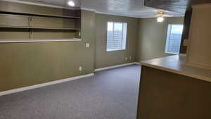 Unfurnished room featuring a ceiling fan, healthy amount of natural light, dark carpet, baseboards, and crown molding