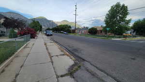 View of asphalt road featuring sidewalks, a mountain view, and curbs