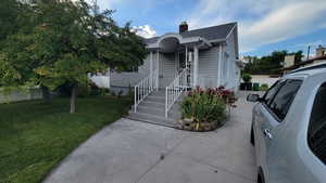 View of front of house with a chimney, a front yard, a shingled roof, and a patio