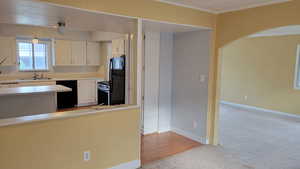Kitchen with black appliances, a sink, light carpet, arched walkways, and light countertops