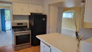 Kitchen featuring stainless steel range with gas stovetop, freestanding refrigerator, under cabinet range hood, white cabinets, and healthy amount of natural light