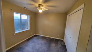 Unfurnished bedroom with dark colored carpet, baseboards, a closet, and a ceiling fan