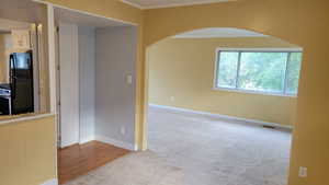 Carpeted spare room featuring arched walkways, ornamental molding, and baseboards