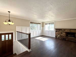Unfurnished living room featuring a textured ceiling, a chandelier, wainscoting, dark wood-style floors, and a decorative wall