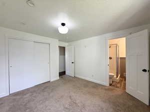 Unfurnished bedroom with carpet, a closet, a textured ceiling, connected bathroom, and baseboards