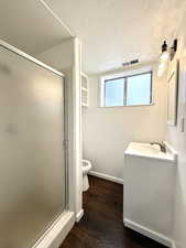 Full bathroom featuring vanity, wood finished floors, toilet, a shower stall, and a textured ceiling