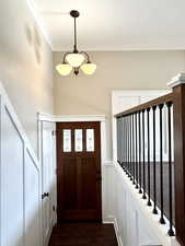 Entryway with crown molding, a chandelier, and dark wood-style flooring