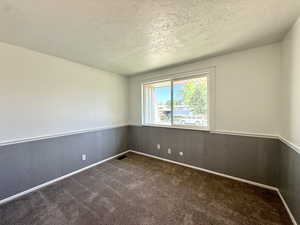 Carpeted empty room with a textured ceiling and a wainscoted wall