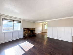 Unfurnished living room with a textured ceiling, a decorative wall, dark wood-style flooring, ornamental molding, and a fireplace