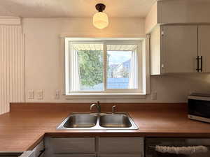 Kitchen featuring stainless steel microwave, a sink, dishwasher, gray cabinets, and a textured ceiling