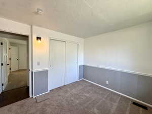 Unfurnished bedroom featuring carpet flooring, wainscoting, a textured ceiling, and a closet