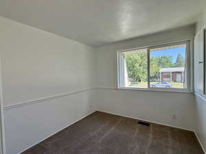 Empty room with dark colored carpet, baseboards, and a textured ceiling