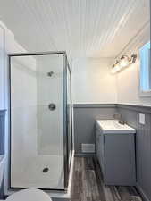 Full bathroom featuring vanity, wood finished floors, a shower stall, a wainscoted wall, and toilet