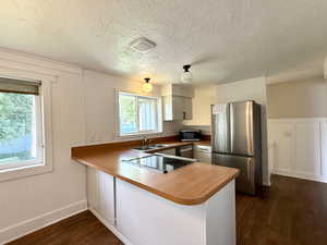 Kitchen featuring stainless steel appliances, a sink, dark wood-style floors, a peninsula, and baseboards