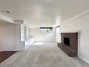 Unfurnished living room featuring a fireplace, carpet flooring, built in shelves, and a textured ceiling